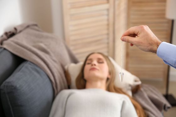Una mujer está recibiendo hipnoterapia mientras una mano sostiene un péndulo sobre ella.