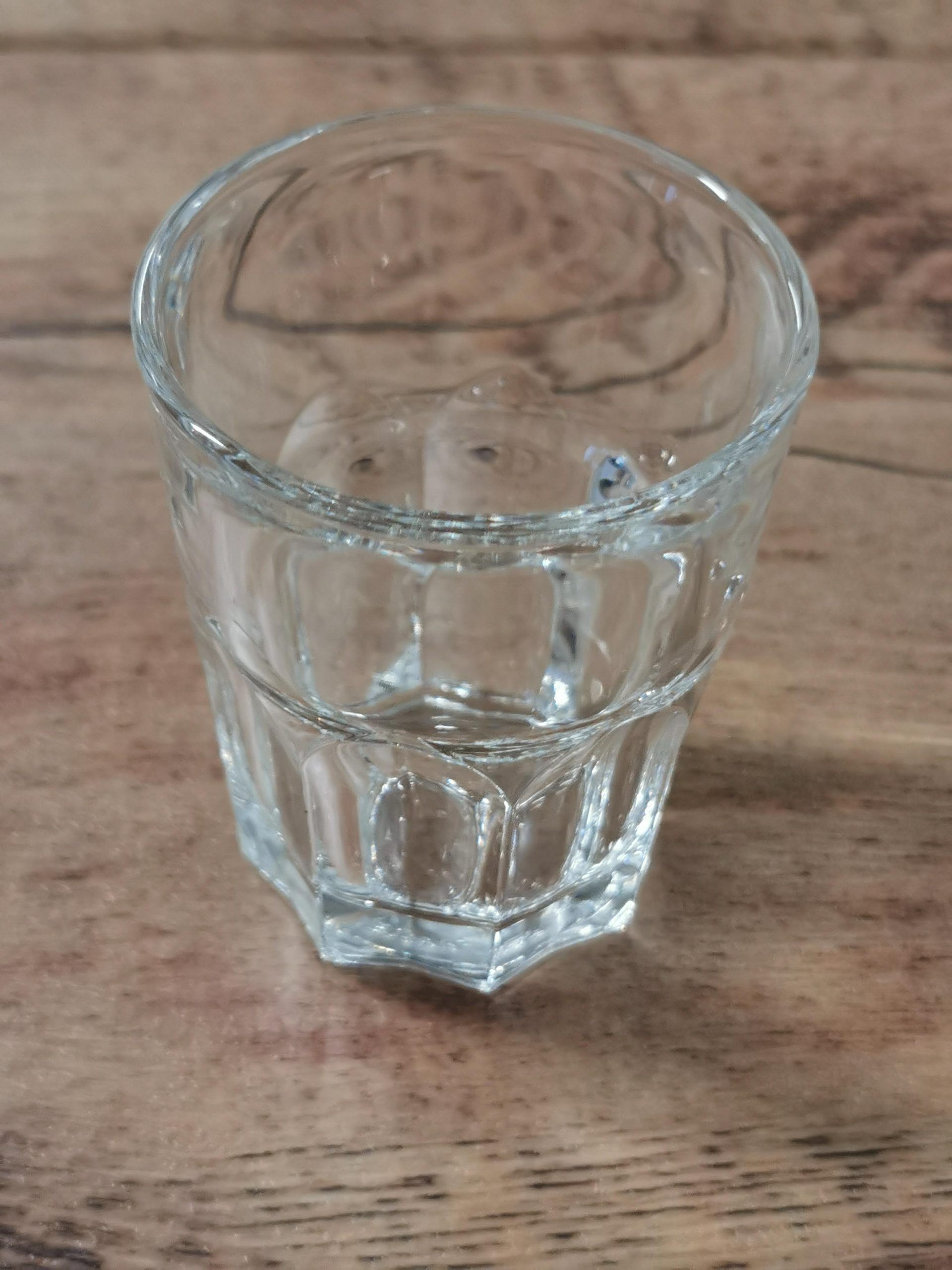 Kirkas lasi puisella pöydällä, osittain täytetty vedellä.