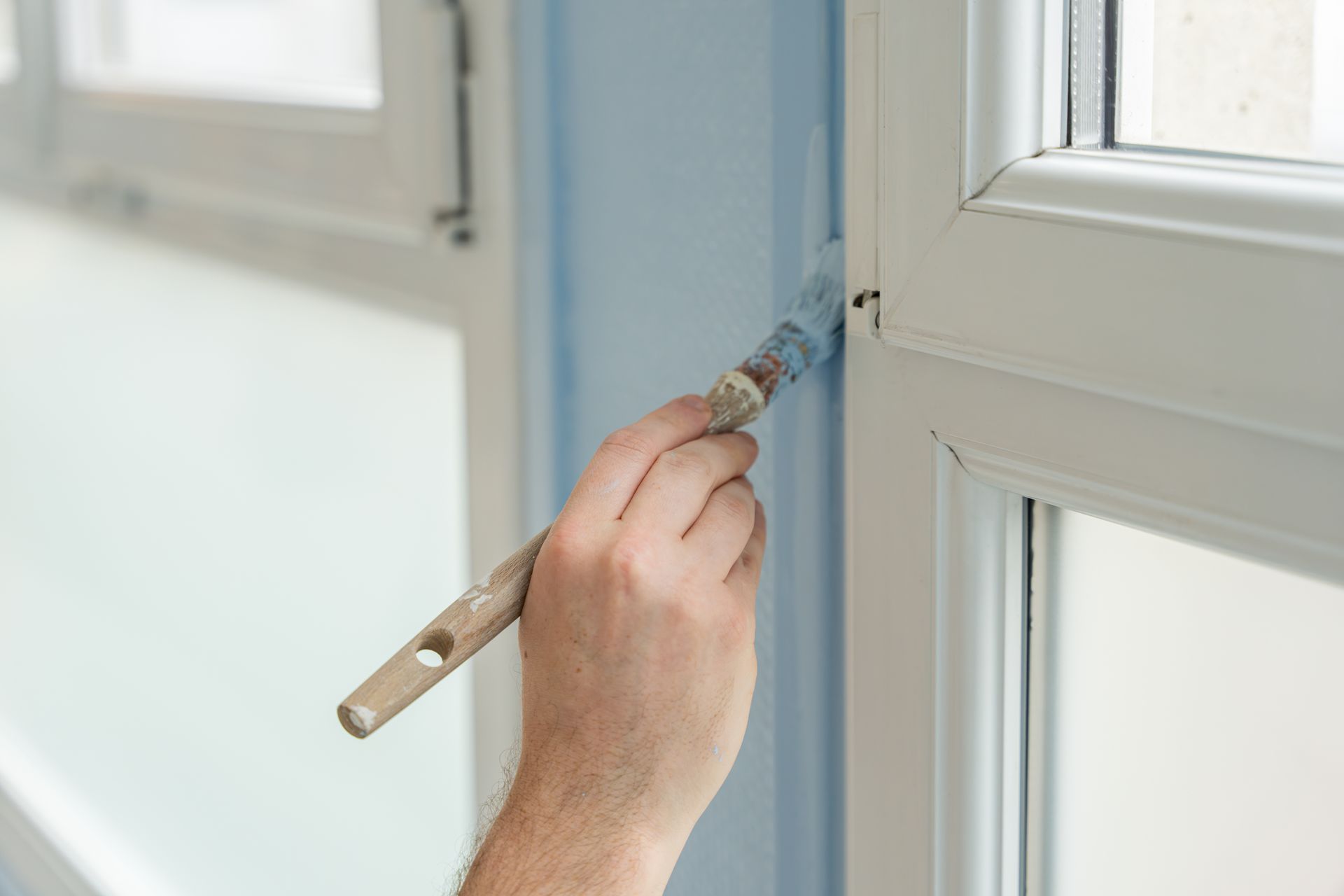 Personne peignant le cadre d'une fenêtre en bleu avec un pinceau.