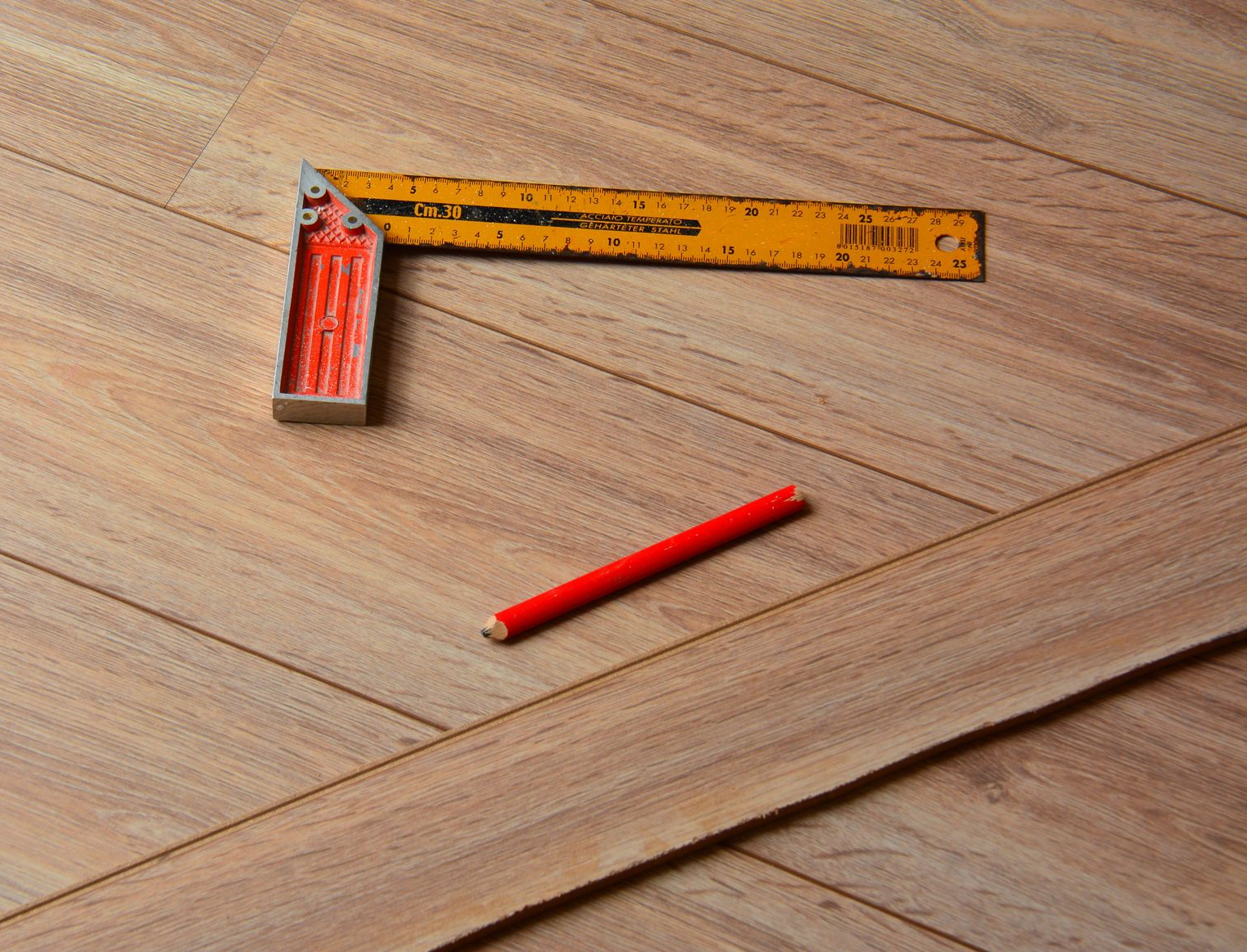 Carré jaune, crayon rouge et planche de bois sur un plancher en bois, outils pour le travail du bois.