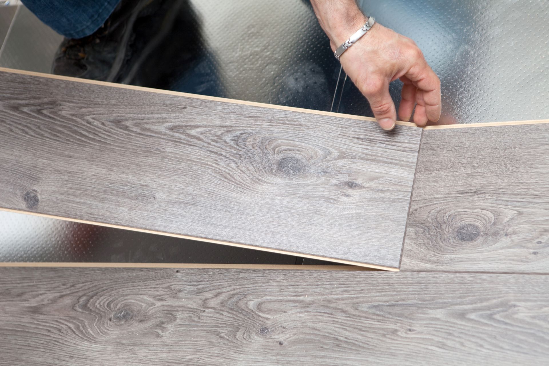 Une main insérant une planche imitation bois gris dans une rangée de parquet installé.