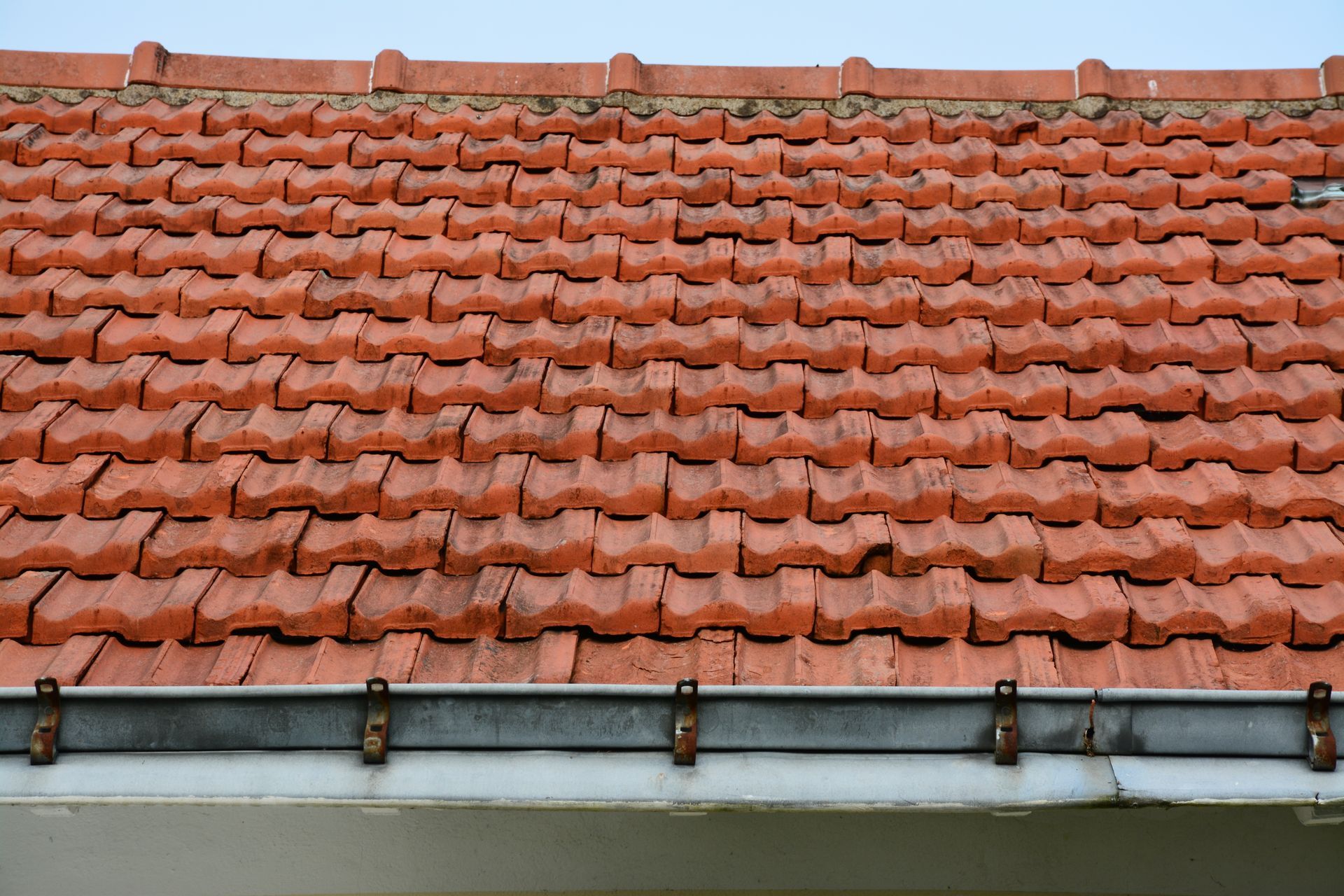 Personne portant des gants noirs installant des tuiles en terre cuite.
