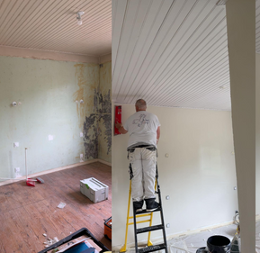 Un monsieur pose du papier peint sur le mur d'une pièce