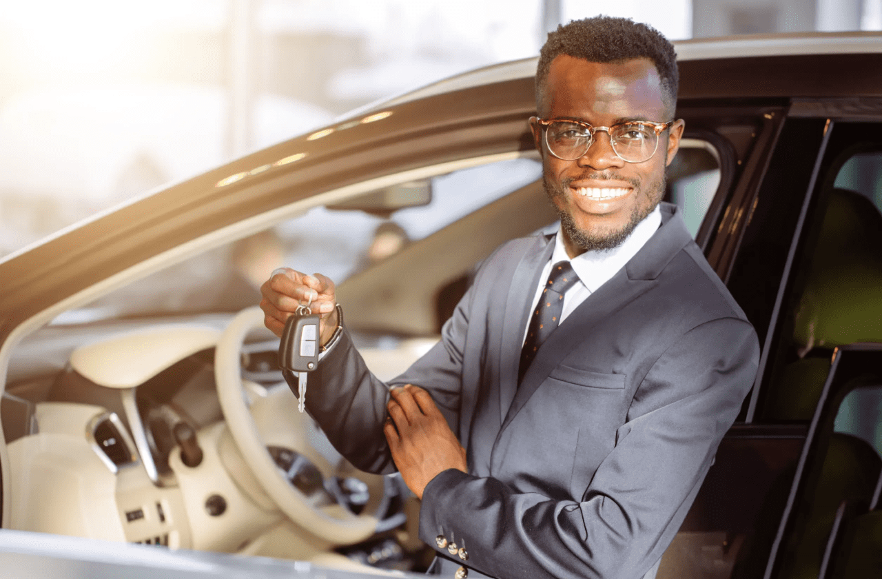 a man in a suit holds a car key in front of a car