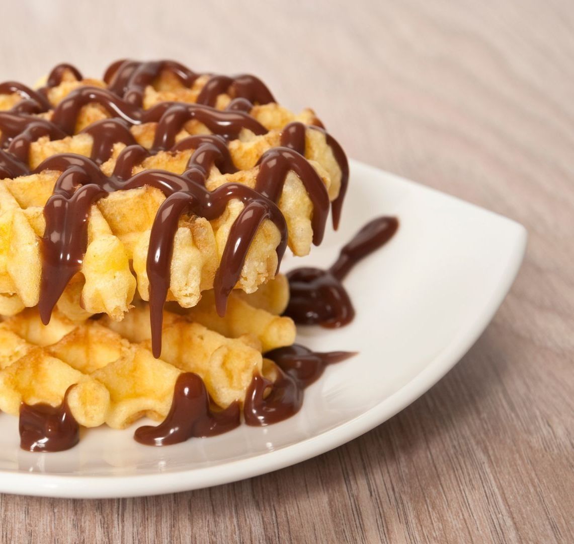 Un plato blanco cubierto con waffles y salsa de chocolate.