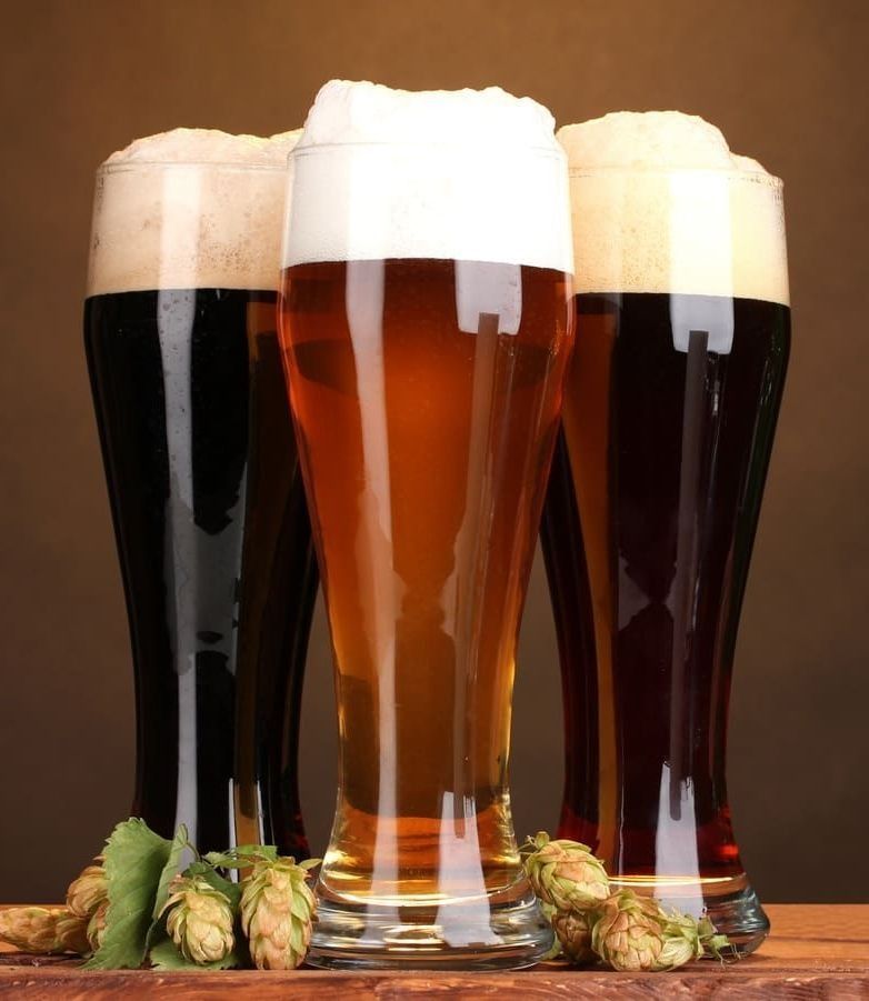 Tres vasos de diferentes tipos de cerveza están sobre una mesa de madera.