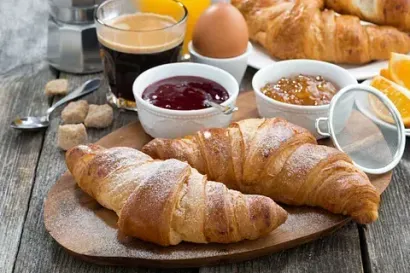 Una tabla de cortar de madera cubierta con croissants, mermelada, huevos, café y jugo de naranja.
