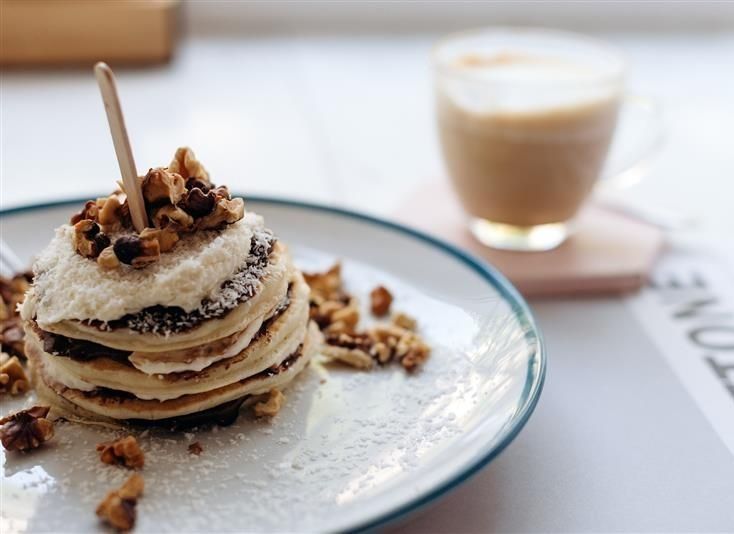 Una pila de panqueques con crema batida y nueces en un plato junto a una taza de café.