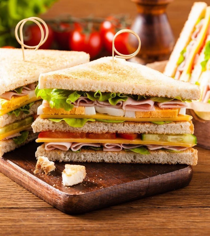 Tres sándwiches se apilan uno encima del otro sobre una tabla de cortar de madera.