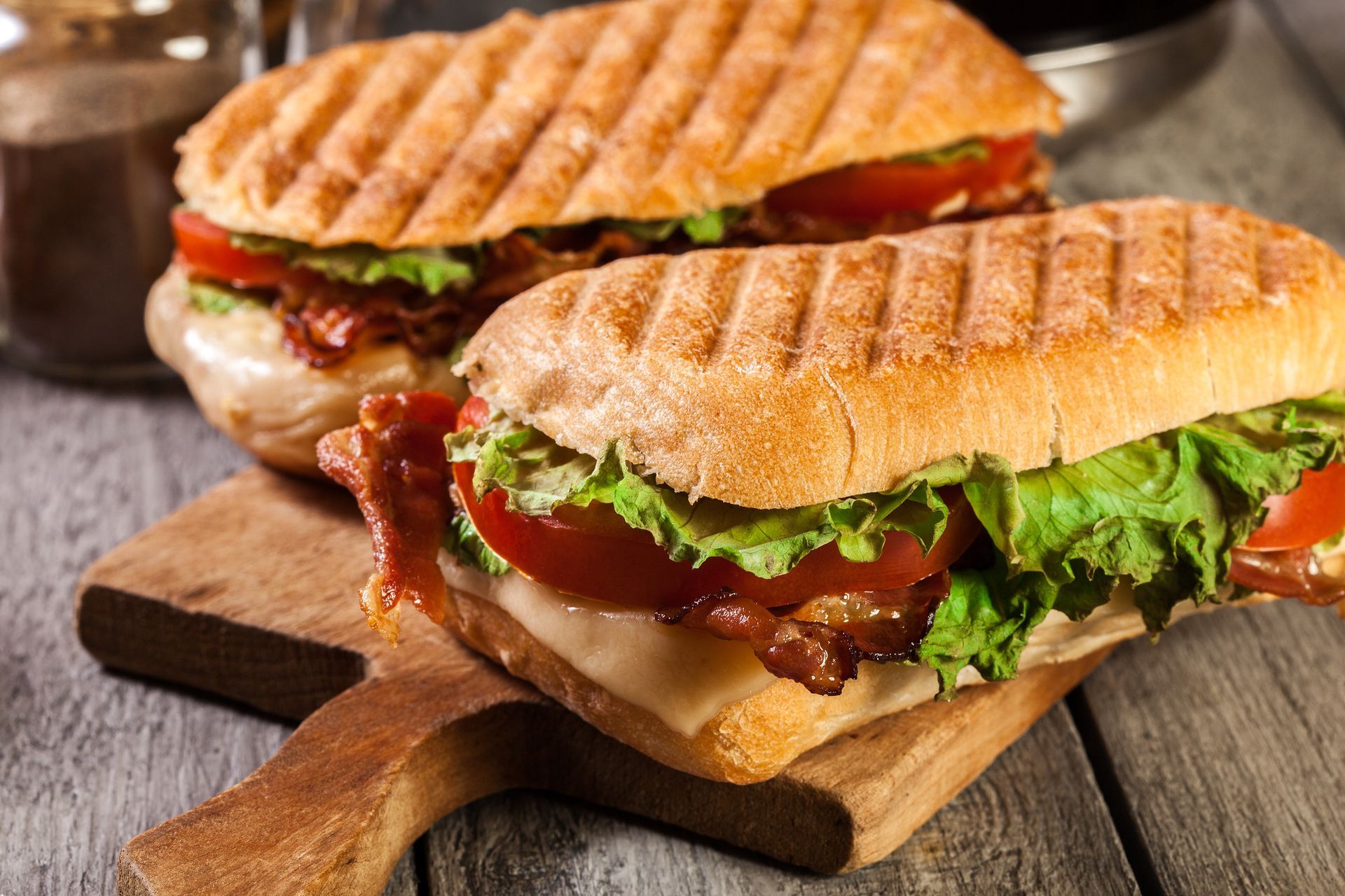 Deux sandwichs grillés avec laitue, tomate et bacon sur une planche en bois.