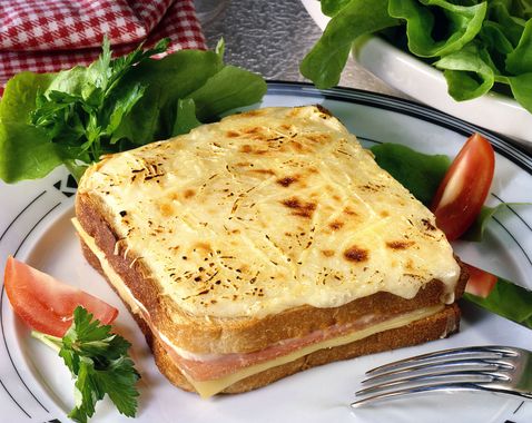 Croque-monsieur grillé garni de fromage fondu, servi sur une assiette avec de la laitue et des tomates en garniture.