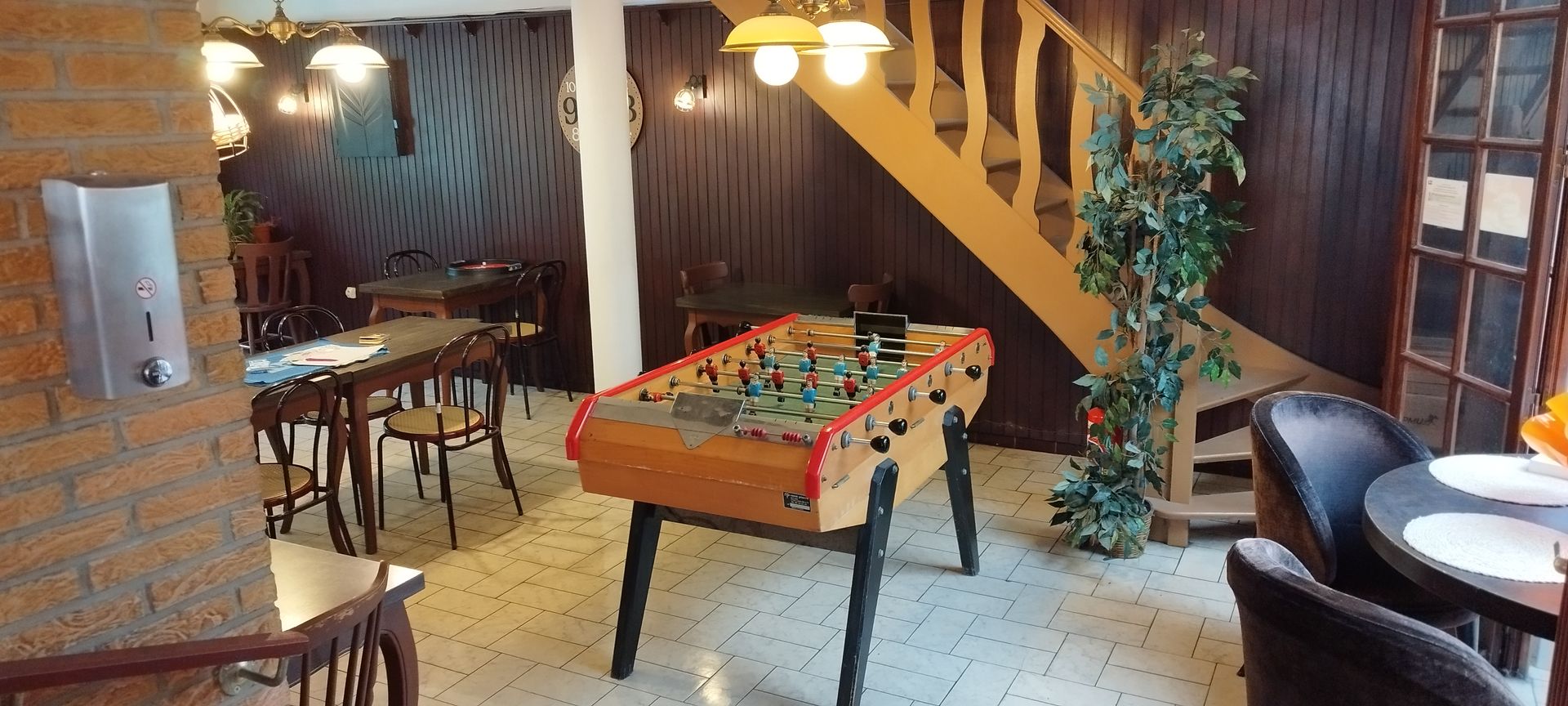Salle de jeux avec baby-foot, coin repas, escalier et éclairage chaleureux.