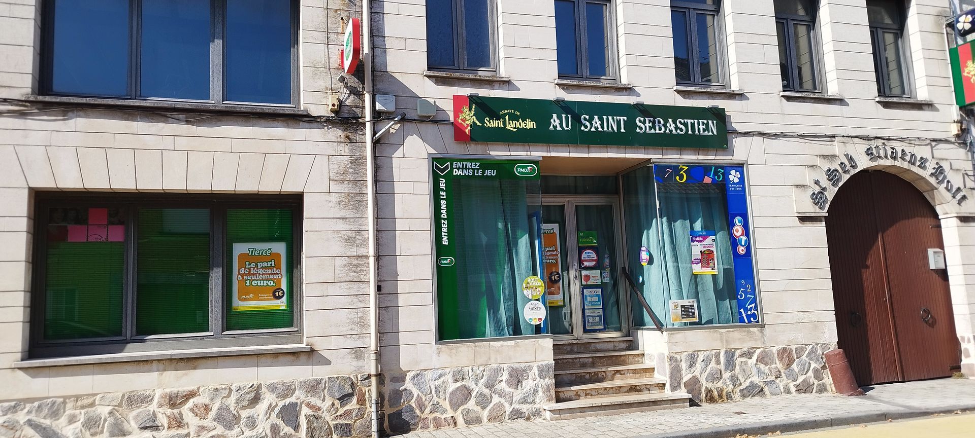 Façade commerciale au rez-de-chaussée avec auvent, vitrines et façade en pierre.