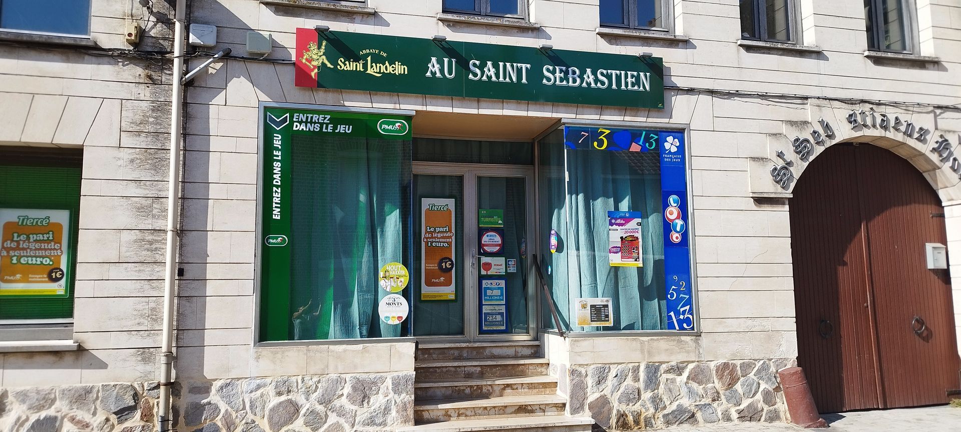Façade de magasin avec auvent et vitrines sur un bâtiment en pierre, à côté d'une porte cintrée.