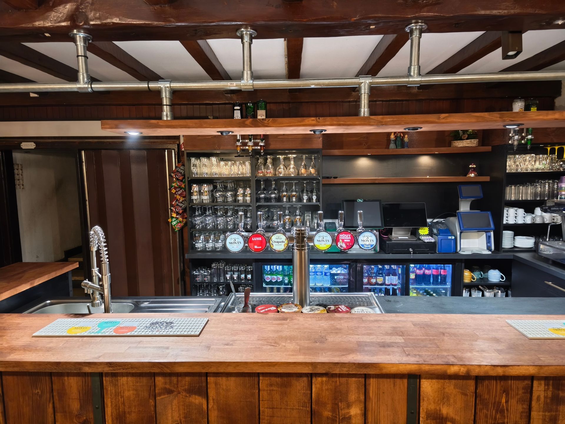 Bar vide avec comptoir en bois, tireuses à bière et étagères de bouteilles derrière.