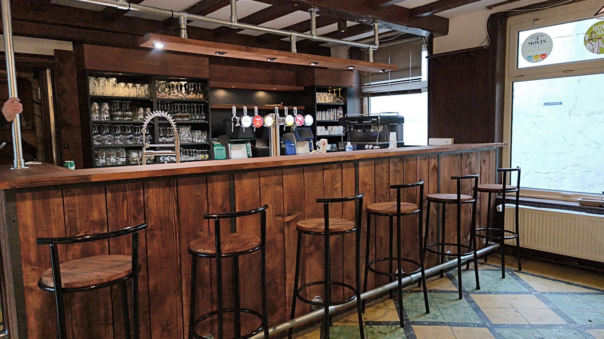 Bar de pub vide avec comptoir en bois, tabourets, étagères à bouteilles et grandes fenêtres