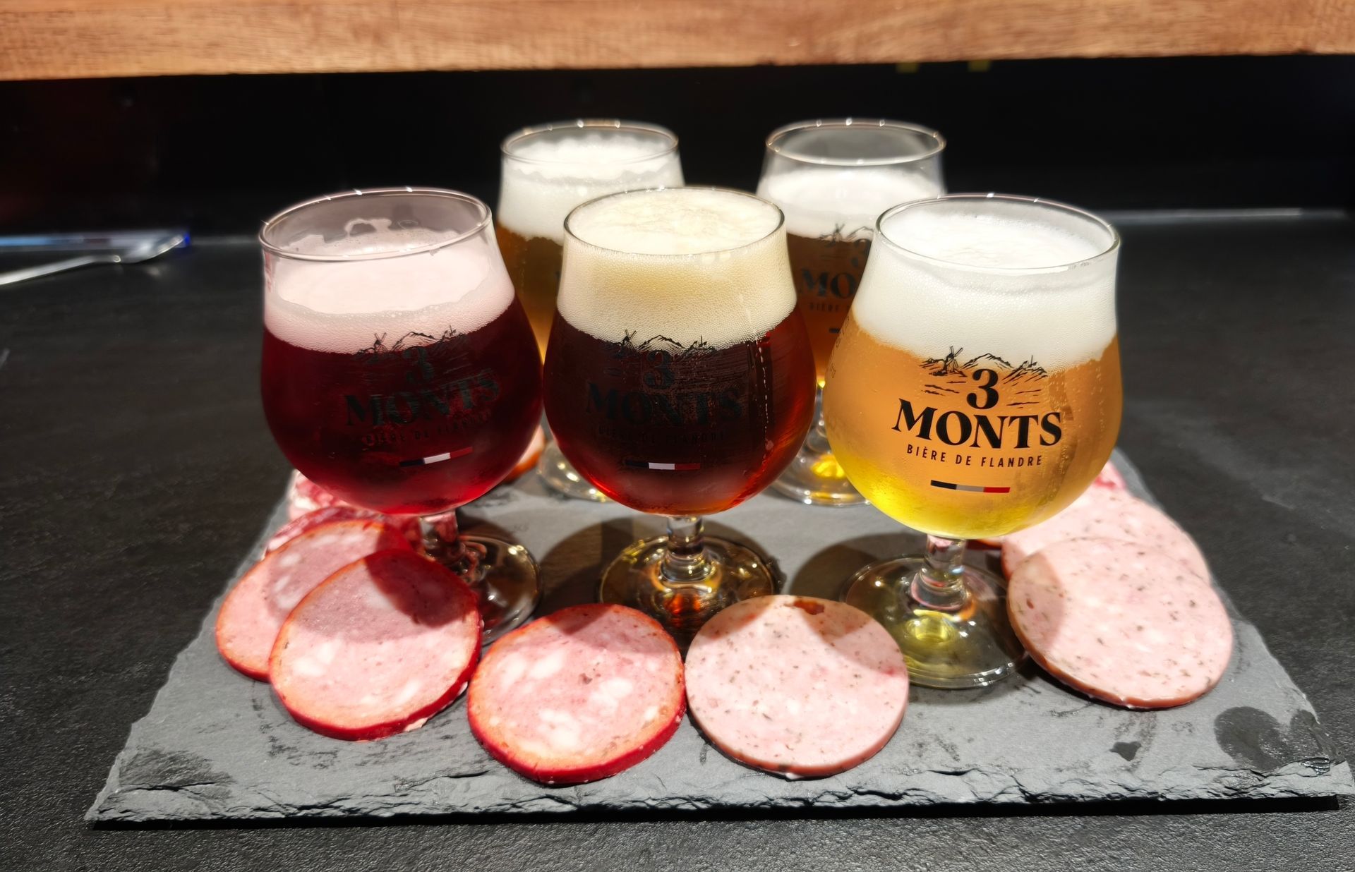 Quatre verres à bière sur une ardoise avec des tranches de salami