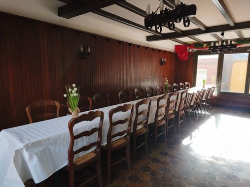 Une longue table à manger est dressée pour une réunion dans une pièce lambrissée, avec des chaises et de la lumière naturelle entrant par les fenêtres.