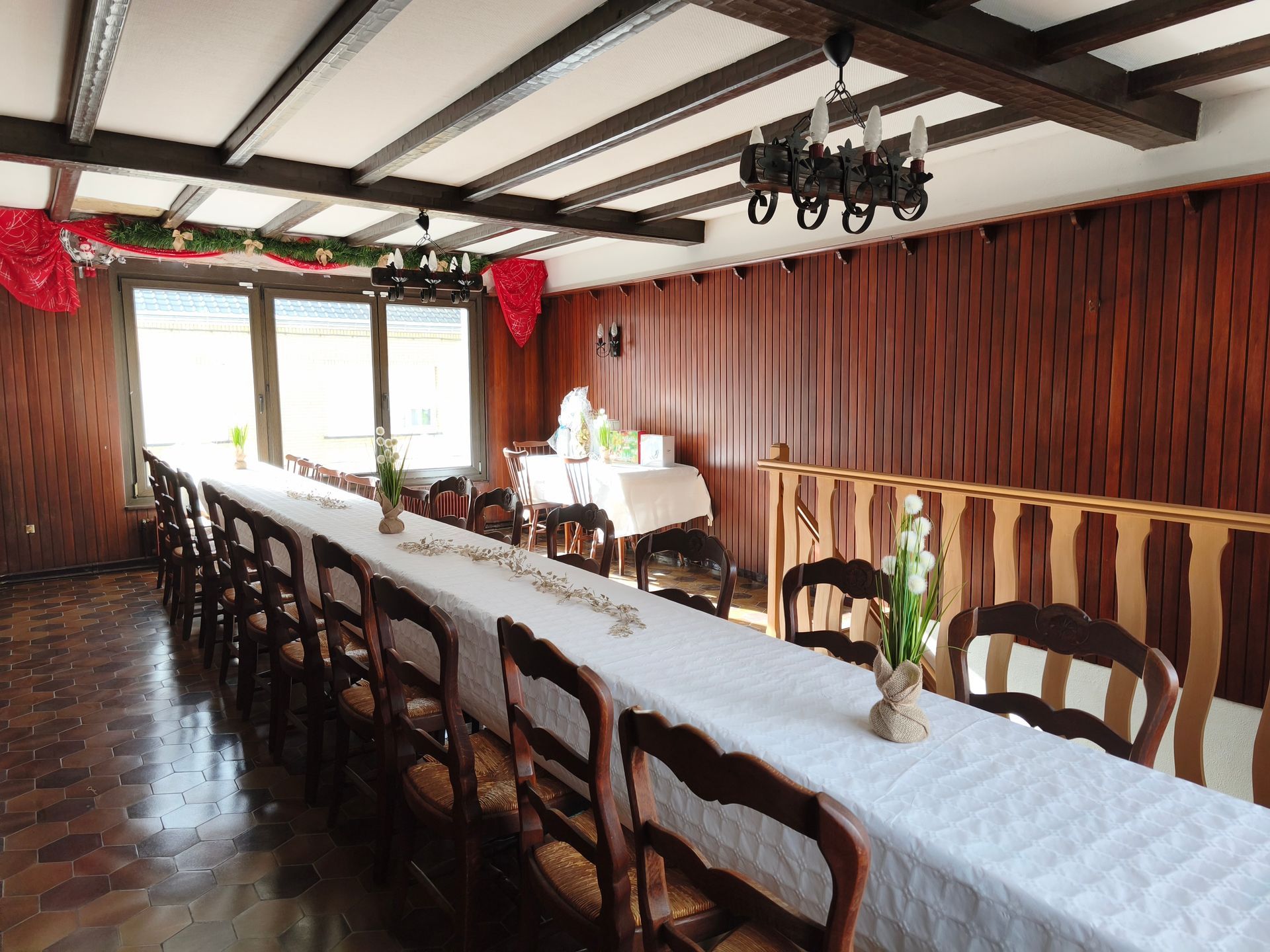 Longue table de banquet dans une salle à manger rustique avec poutres en bois et rideaux.