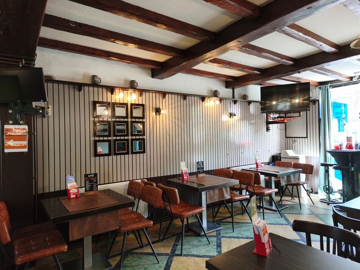 Intérieur d'un petit café avec tables et bancs, murs rayés, luminaires suspendus et une fenêtre.