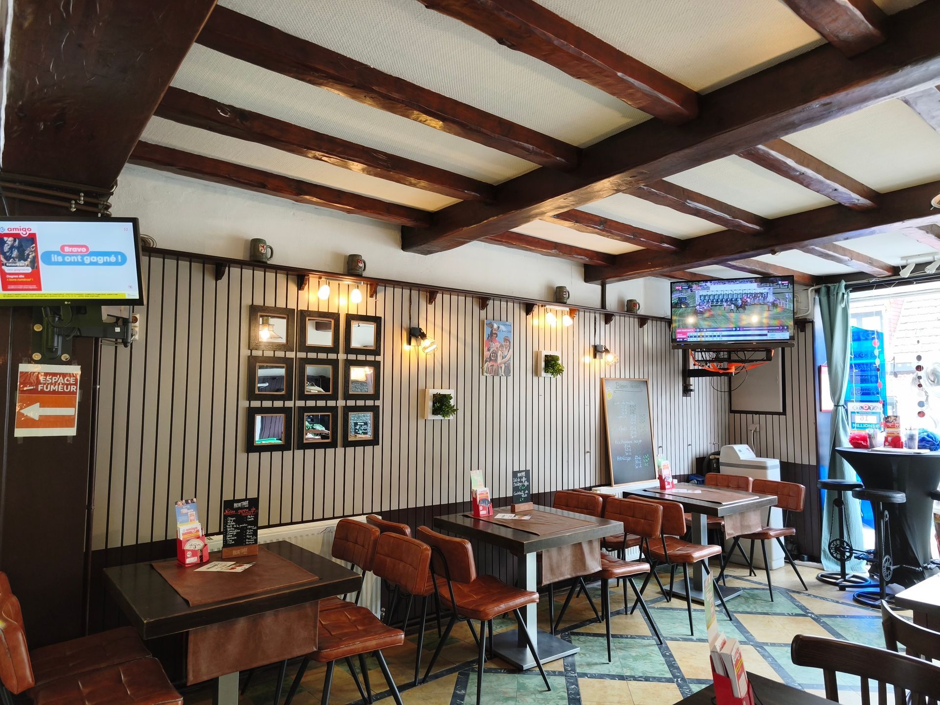 Intérieur vide d'un restaurant rustique avec tables en bois, décoration murale et écrans de télévision sous des poutres apparentes au plafond.