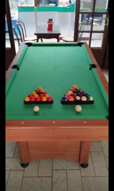 Deux tables de billard avec boules et queues rangées dans une salle de billard.