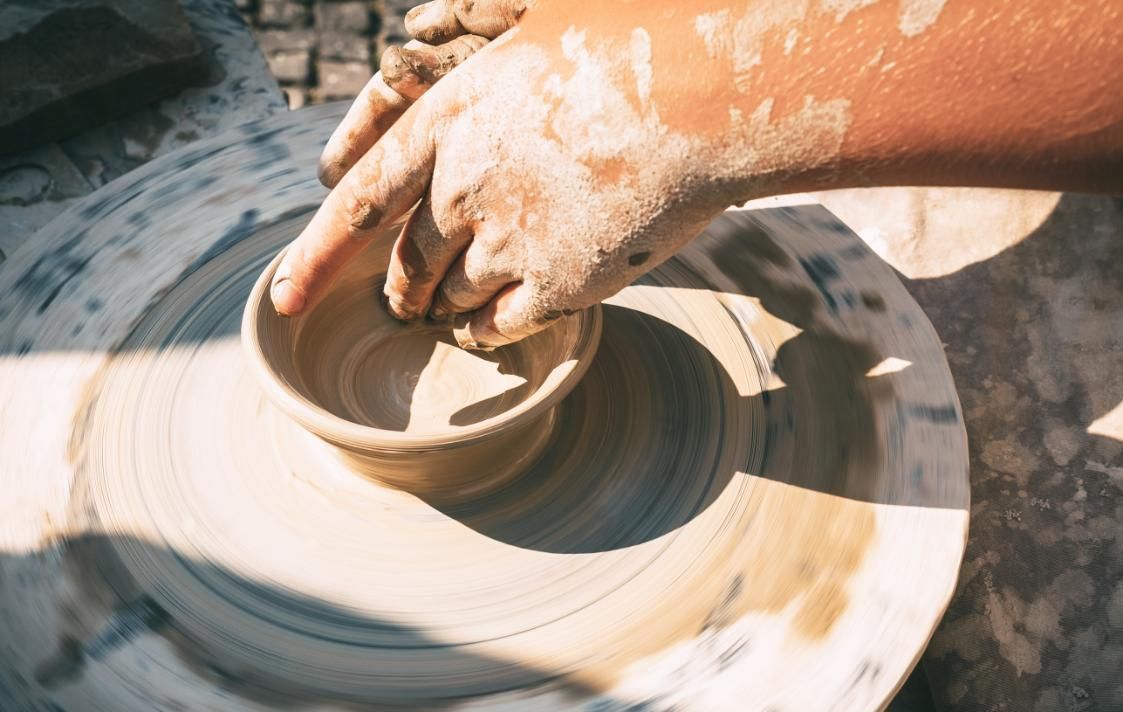 Manos moldeando un cuenco de cerámica en un torno. Se aprecia arcilla en las manos y el torno.
