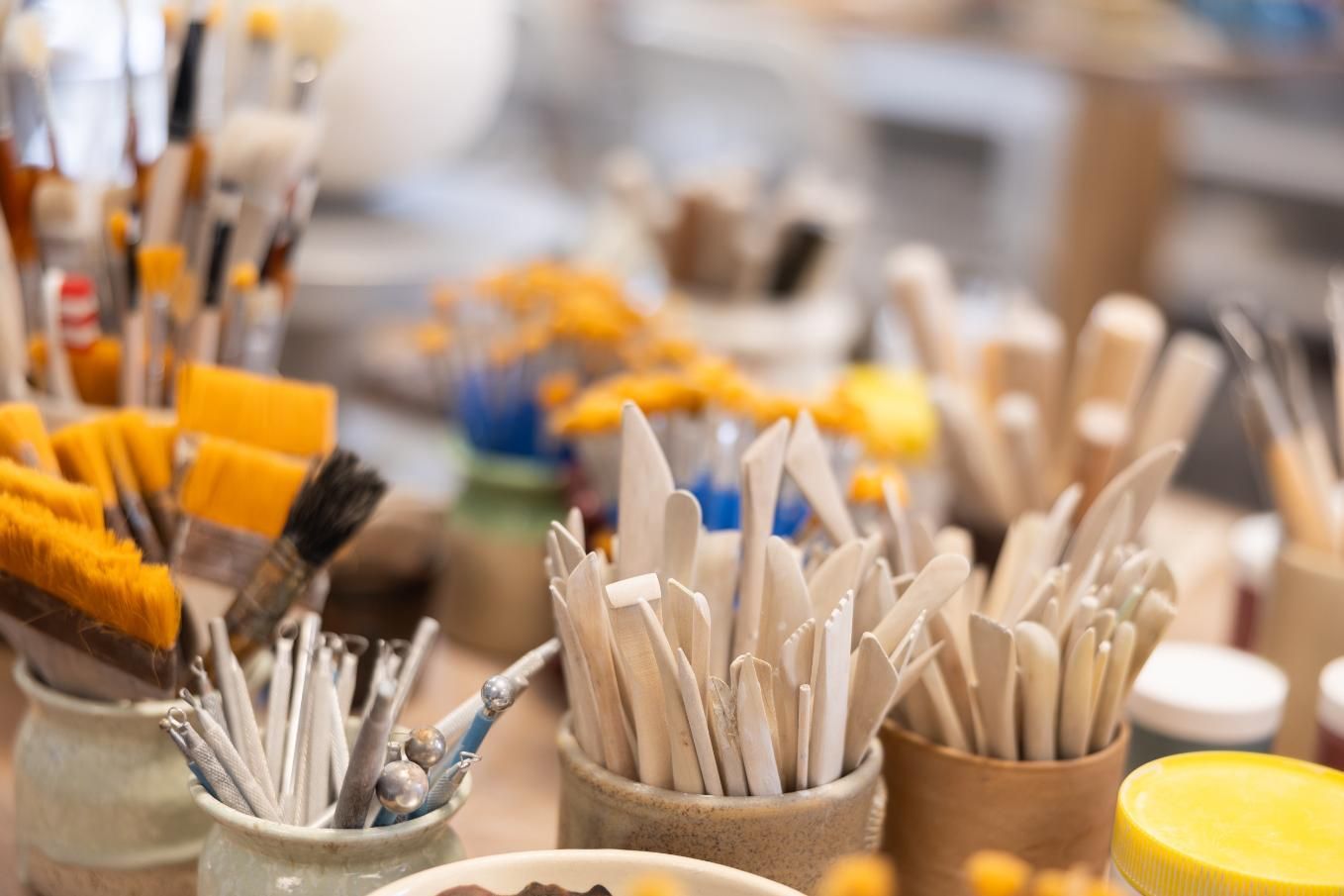Materiales de arte en frascos: pinceles, herramientas y materiales sobre una mesa, entorno de estudio.