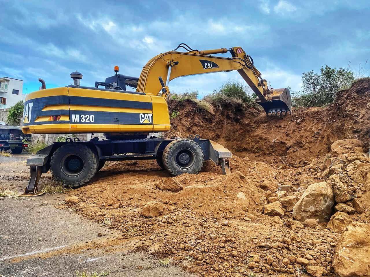 Excavadora amarilla cavando un montículo de tierra en una obra de construcción bajo un cielo azul.