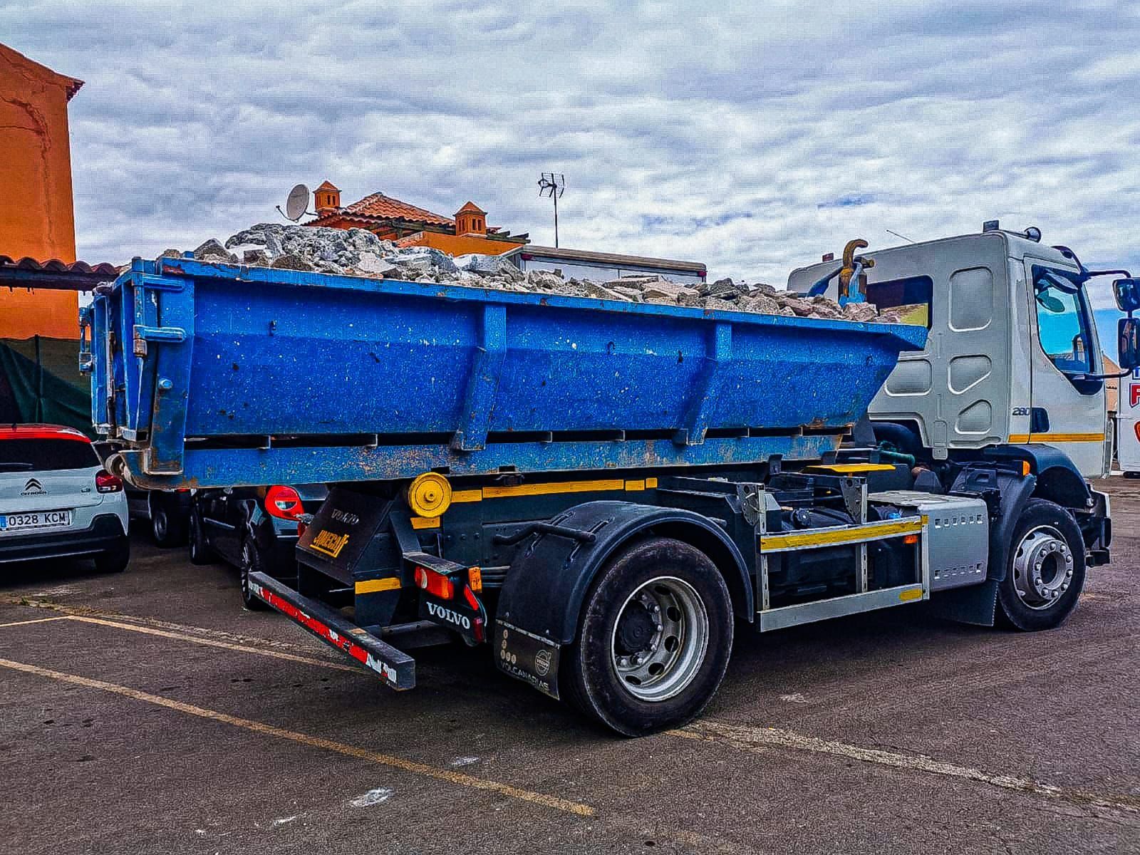 Un camión volquete con un contenedor de basura azul en la parte trasera está estacionado en un estacionamiento.