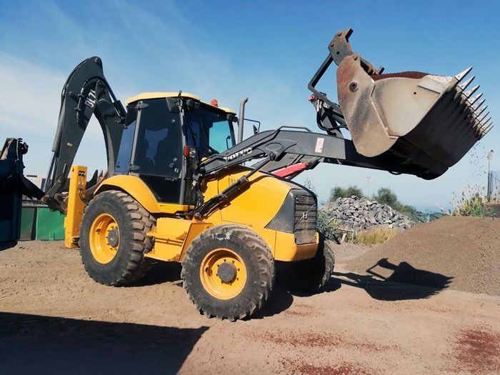 Una retroexcavadora amarilla está encima de un montón de tierra.
