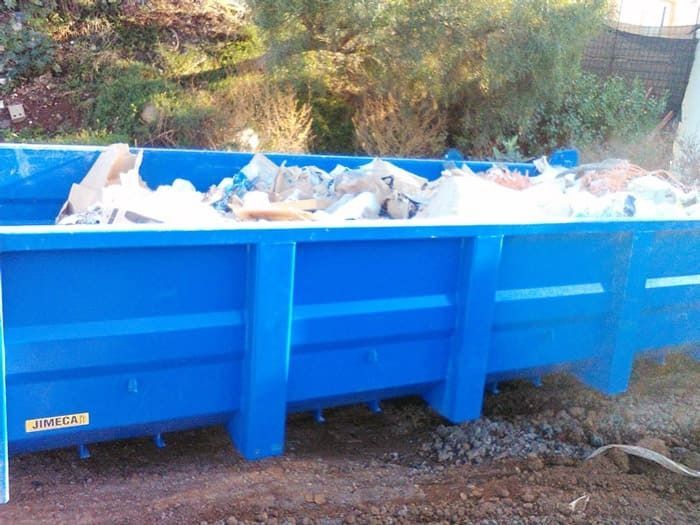 Un contenedor azul lleno de basura está en el suelo.