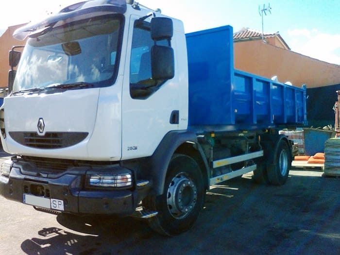 Un camión volquete blanco con una caja azul está estacionado frente a un edificio.