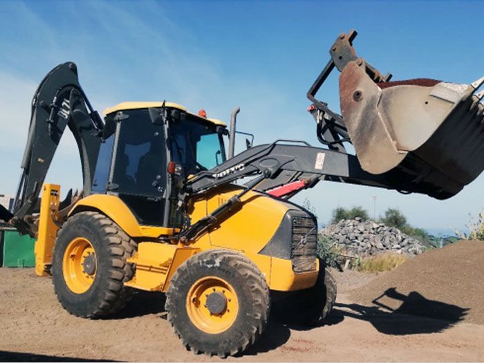 Un tractor amarillo con un cucharón grande está sentado en un montón de tierra.