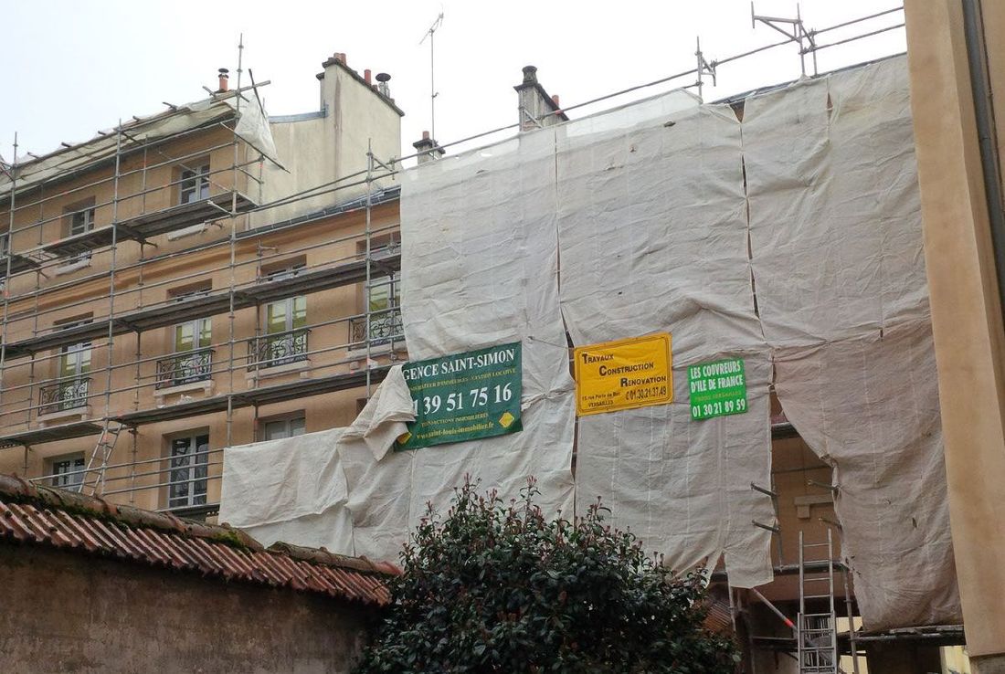 Un échafaudage recouvert d'une bâche blanche à côté d'un immeuble d'appartements.