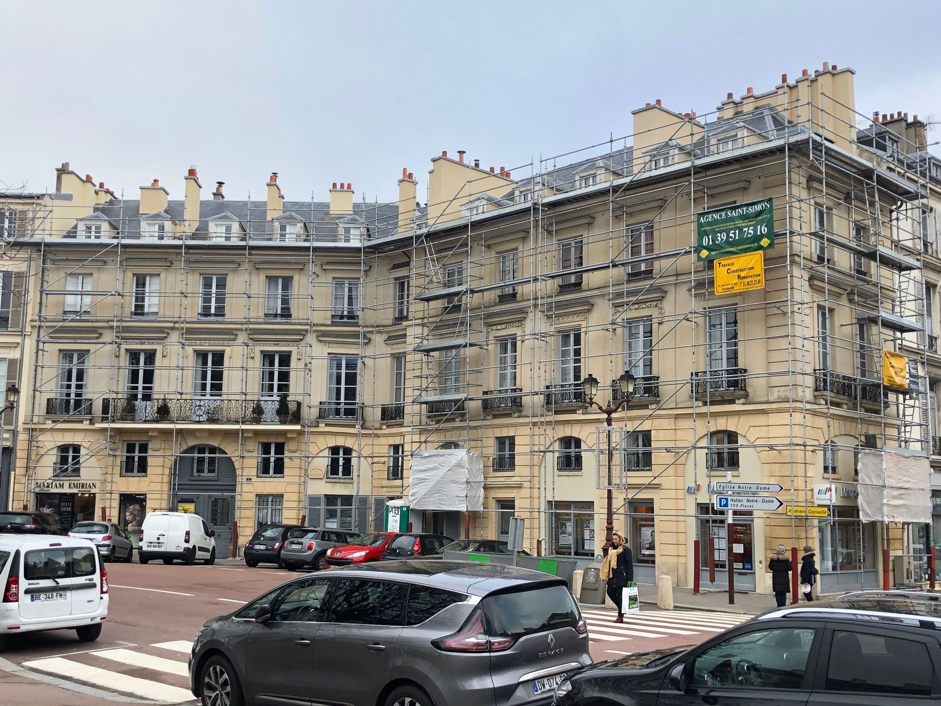 Bâtiments en pierre dans une rue à Paris, avec des voitures garées et des piétons sous un ciel nuageux