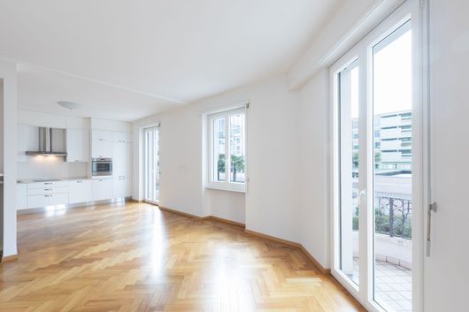 Un appartement vide avec un parquet et des grandes fenêtres donnant sur un balcon