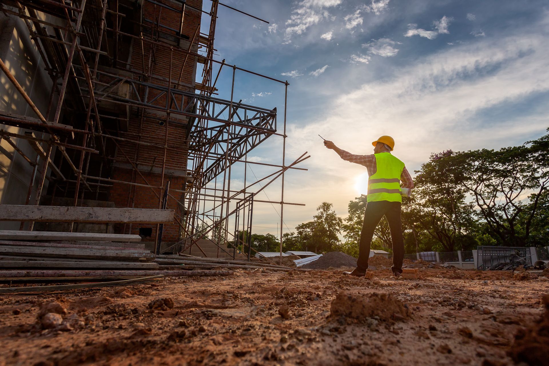 Un ouvrier du bâtiment, vêtu d'un gilet fluorescent et d'un casque de chantier se trouve près d'un chantier de construction