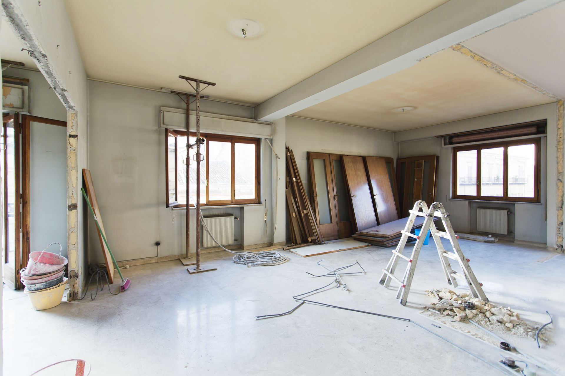 Chantier de rénovation avec une pièce inachevée, des fenêtres, des outils éparpillés au sol.