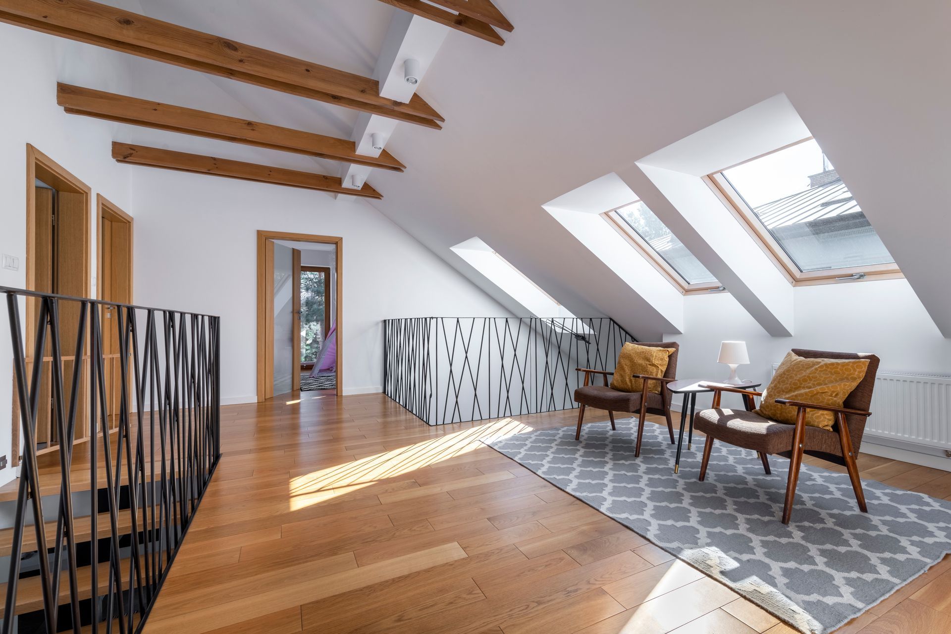 Chambre mansardée lumineuse avec puits de lumière inclinés, tapis à motifs et deux fauteuils près d'une fenêtre.