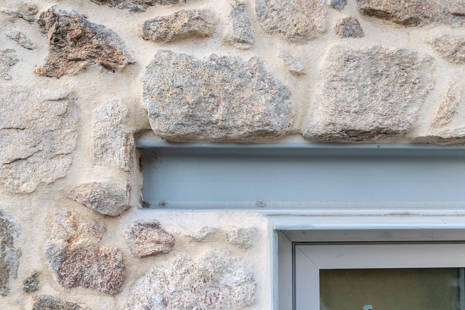 Mur extérieur en pierre avec une fenêtre à cadre blanc sous un linteau