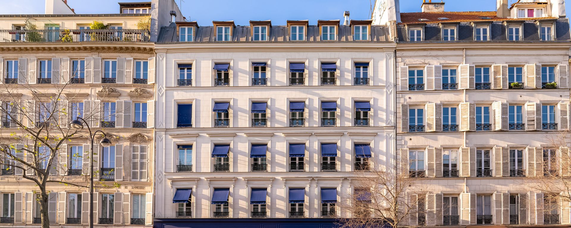 Façade d'immeuble parisien en pierre, volets bleus et balcons en fer forgé