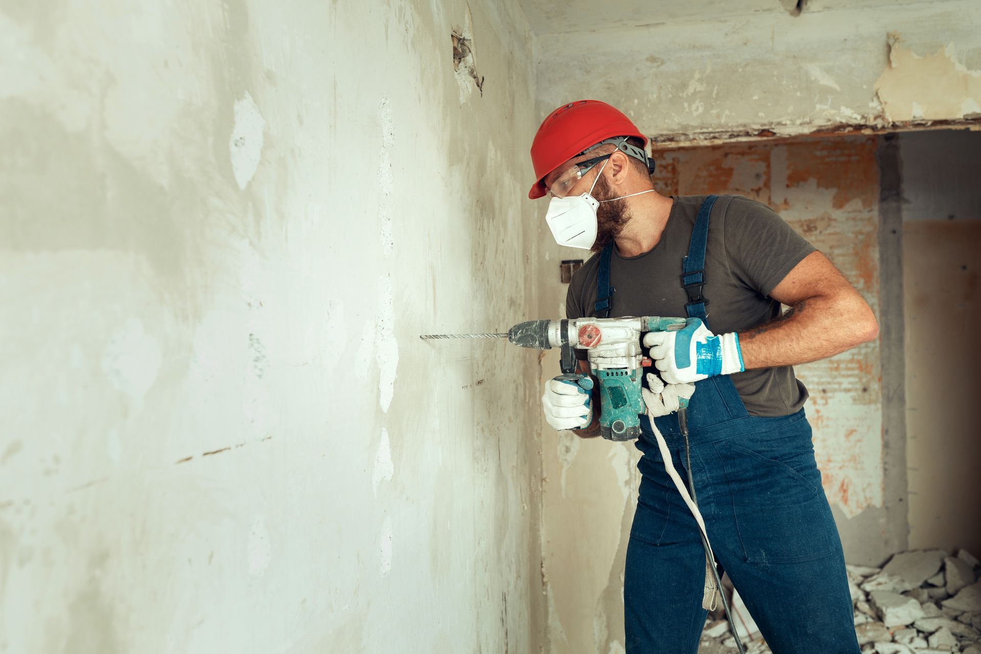 Ouvrier du bâtiment portant un casque rouge perçant un mur