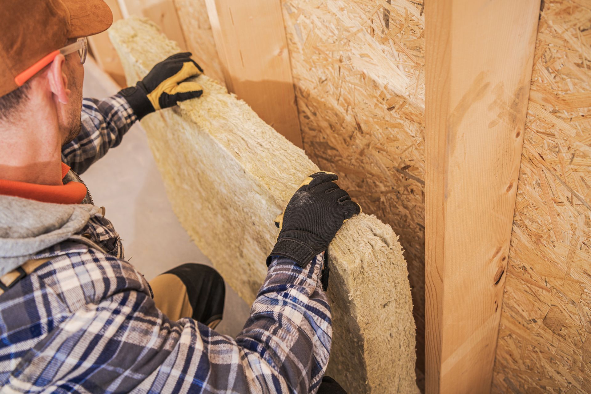 Personne installant des rouleaux d'isolant à l'intérieur d'une ossature murale en bois