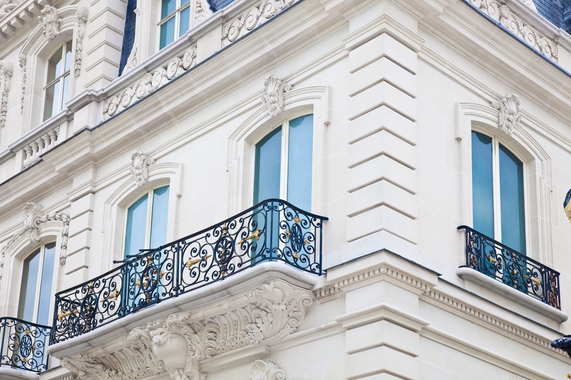 Immeuble blanc d'angle avec fenêtres bleues et balcons en fer forgé noir ouvragés