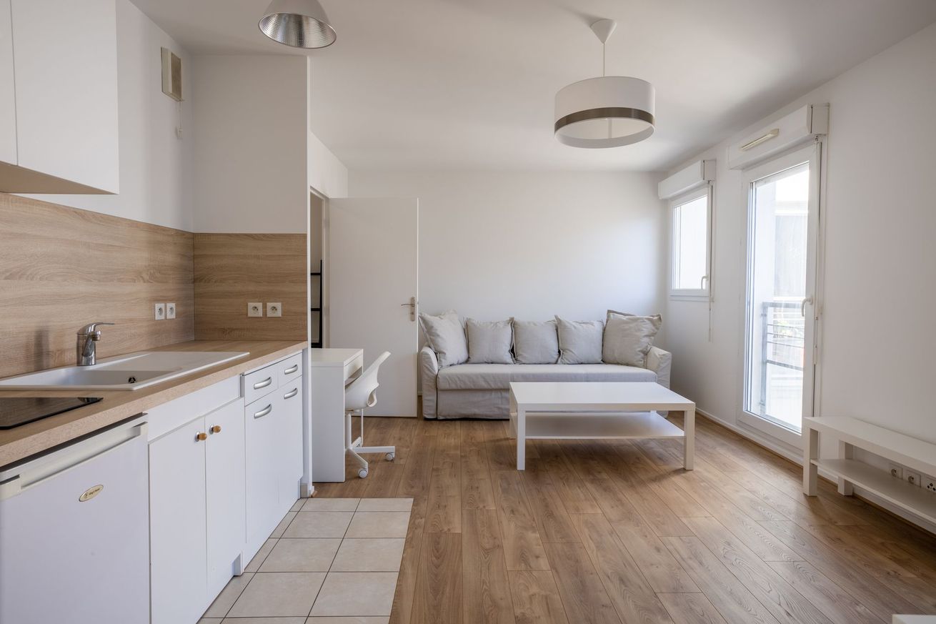 Studio moderne et lumineux avec cuisine, canapé et portes-fenêtres donnant sur un balcon
