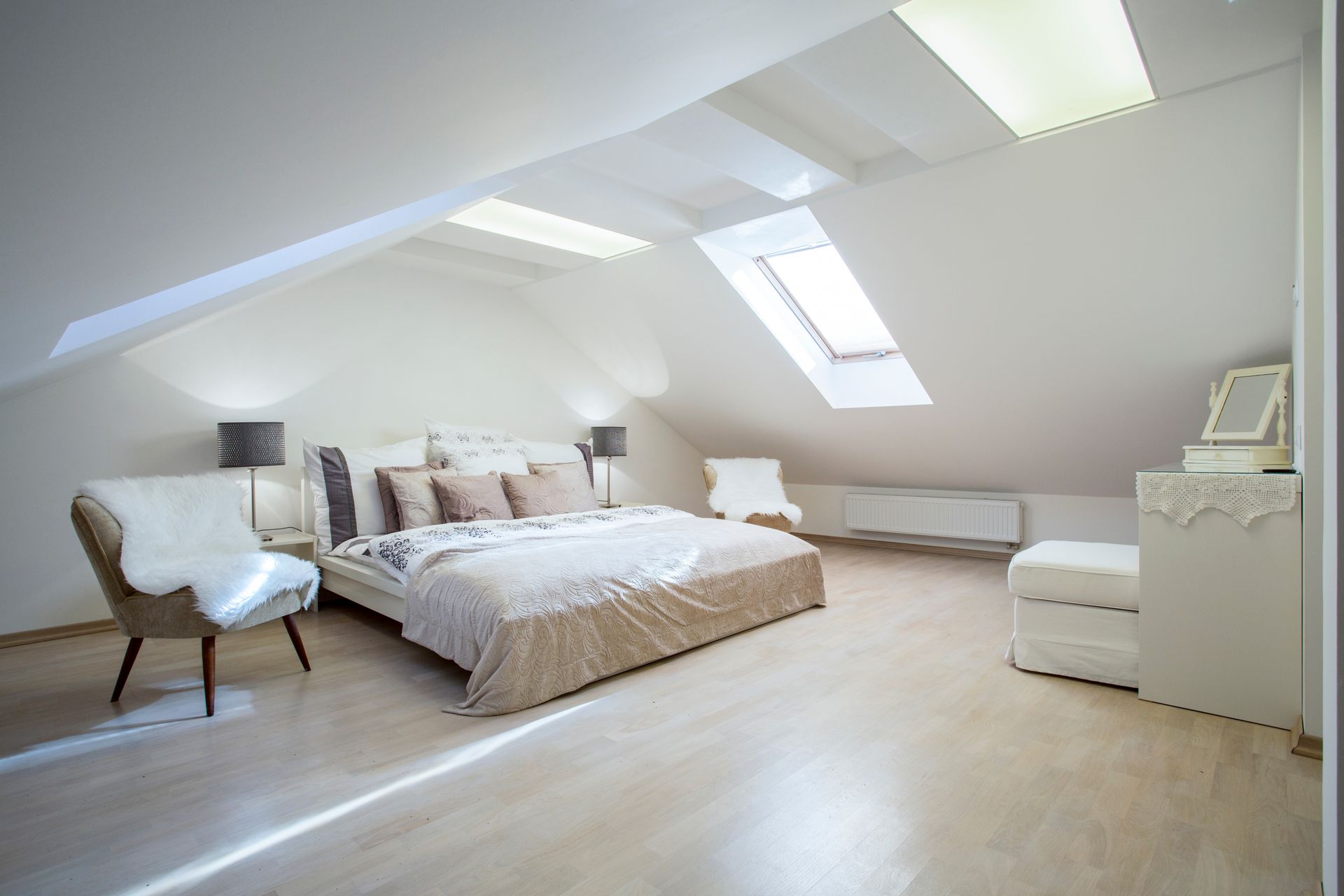 Chambre mansardée lumineuse avec un lit et un puits de lumière au-dessus.