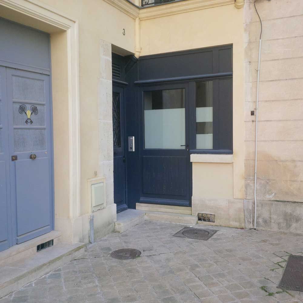 Porte d'entrée bleue et entrée latérale donnant sur une ruelle étroite pavée, avec des murs rénovés.