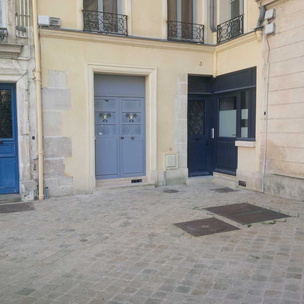 Entrée d'un immeuble avec une double porte bleue et une porte sombre à côté.