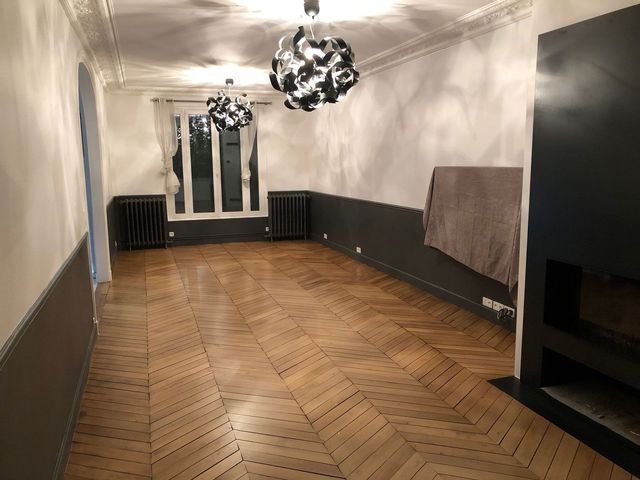 Pièce avec un parquet en chevrons, murs blancs, lambris noir en partie basse et suspensions.